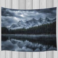 the mountains are covered with clouds and trees in front of a lake that is surrounded by wood