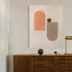 an abstract painting hangs on the wall above a dresser