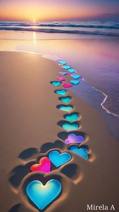 a long line of hearts drawn in the sand at the beach with sunset behind them