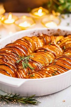 a casserole dish filled with sliced potatoes and topped with rosemary sprigs