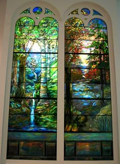 two stained glass windows in a church with trees and water on the window sill