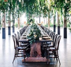 a long table with chairs and greenery on it