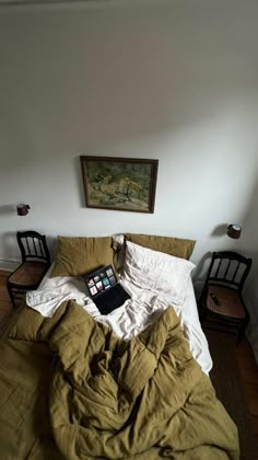 an unmade bed with a laptop on top of it in a room next to two chairs