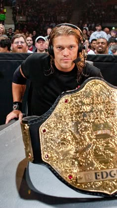 a man with headphones standing in front of a large gold wrestling belt on top of a table