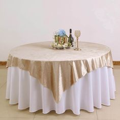 a round table with a champagne bottle and two wine glasses on it, sitting in front of a white wall