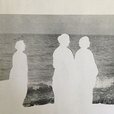 three people standing on the beach looking out at the ocean