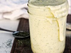 a jar filled with white sauce sitting on top of a wooden table next to a spoon