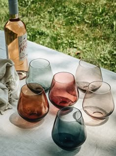 several different colored wine glasses sitting on a table next to a bottle of wine and napkins