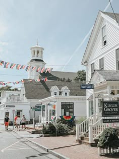 people are walking down the street in front of white buildings with flags hanging from them