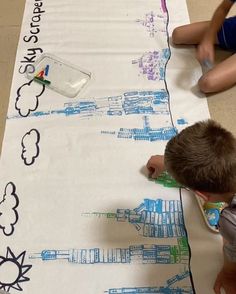 two children are drawing on a large sheet of paper