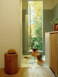 two children are in the bathtub and one is sitting on the floor next to an open door