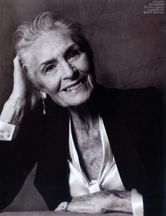 an older woman sitting at a table with her hand on her head and smiling for the camera