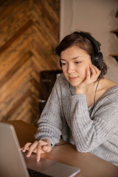 a woman sitting at a table with a laptop computer and headphones on her ears