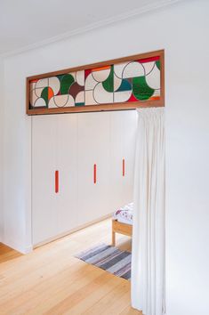 a bedroom with white walls and wooden flooring has colorful artwork on the headboard