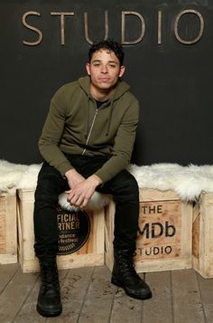 a young man sitting on top of crates in front of a blackboard with the words studio