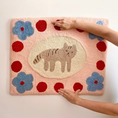 a woman is painting a rug on the wall with flowers and animals in pink, blue, red and white colors