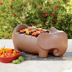 an elephant shaped bbq grill next to a bowl of peppers and carrots on a table