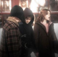 three people standing in front of a window with snow on the ground and one person wearing a hoodie