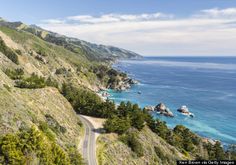 a scenic road on the side of a cliff overlooking the ocean and trees in the foreground