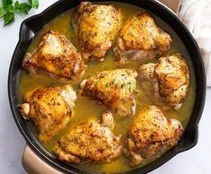 chicken thighs in a skillet with gravy and parsley on the side