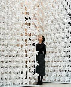 a woman standing in front of a sculpture made of white paper flowers and leaves with her eyes closed