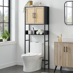 a white toilet sitting next to a wooden cabinet and sink in a room with windows