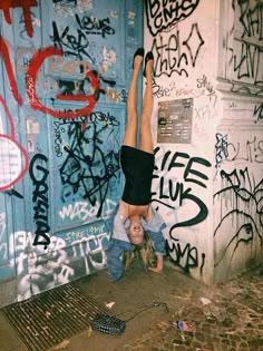 a person doing a handstand in front of a wall with graffiti on it