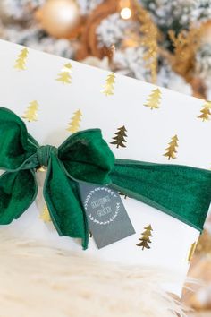 a present wrapped in white paper with a green bow on it, sitting next to a christmas tree