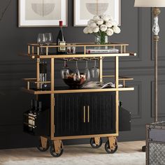 a black and gold bar cart with wine glasses on it in front of two framed pictures