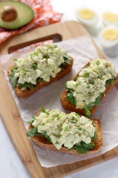 three pieces of bread with cream cheese and avocado on them sitting on a cutting board