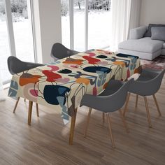 a dining room table covered with a colorful flowered tablecloth next to two gray chairs