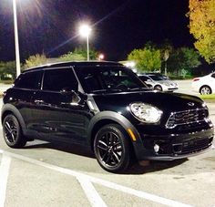 a black mini cooper parked in a parking lot at night with its lights turned on