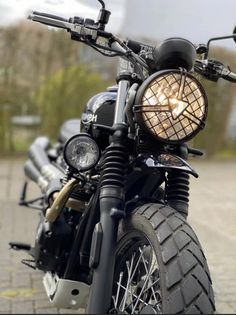 a close up of a motorcycle parked on a brick road with trees in the background