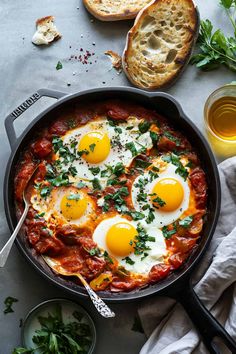 two fried eggs in tomato sauce with bread and parsley on the side next to it