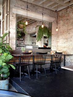 an empty restaurant with tables and chairs in front of a brick wall filled with potted plants