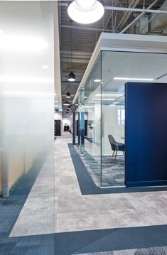 an empty office with glass walls and blue partitions on the wall, carpeted flooring