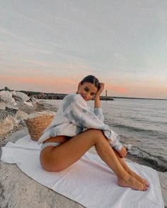 a woman sitting on top of a towel next to the ocean