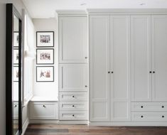 an empty room with white cupboards and pictures on the wall above them, along with hardwood flooring