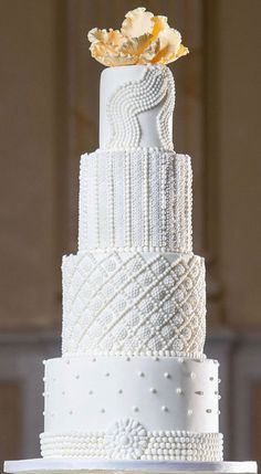 a three tiered white wedding cake with beaded details and a flower on top