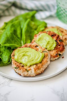 two chicken patties with avocado on a plate next to lettuce