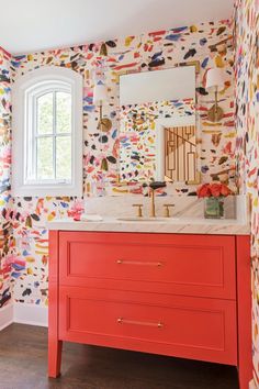 a bathroom with colorful wallpaper and an orange vanity in front of a white window