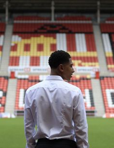 a man standing in front of a soccer field wearing a white shirt and black pants