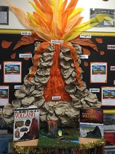 an orange and yellow tree made out of books on top of a shelf in front of a bulletin board