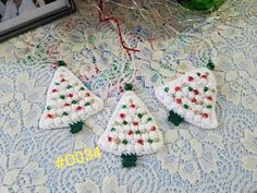 three crocheted christmas tree ornaments on a table next to a framed photo and flowers