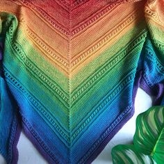 a multicolored knitted sweater sitting on top of a white table next to a green leaf