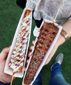 two people holding donuts with sprinkles on them in paper trays