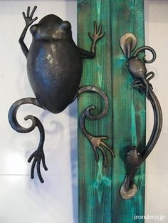 two metal geckos are hanging on the side of a wooden plank with green paint