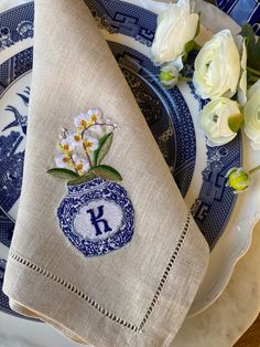 a blue and white plate topped with two napkins covered in embroidered monogrammed flowers