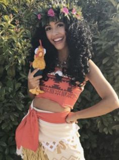 a woman in a hula skirt holding a stuffed animal and smiling at the camera