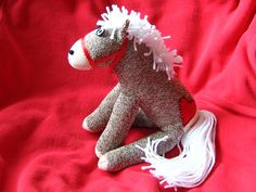 a small stuffed horse sitting on top of a red cloth covered bed sheet with white fringes